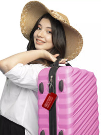 Woman wearing a hat and holding a pink suitcase with a red medical luggage tag attached.